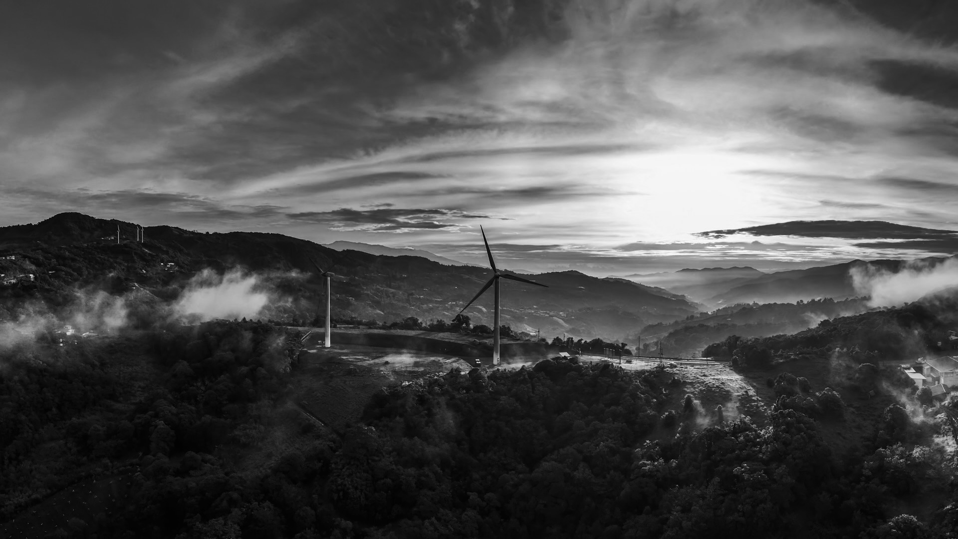 Sumuinen vuoristomaisema, jossa näkyy tuulivoimala aurinkoisessa taivaassa.