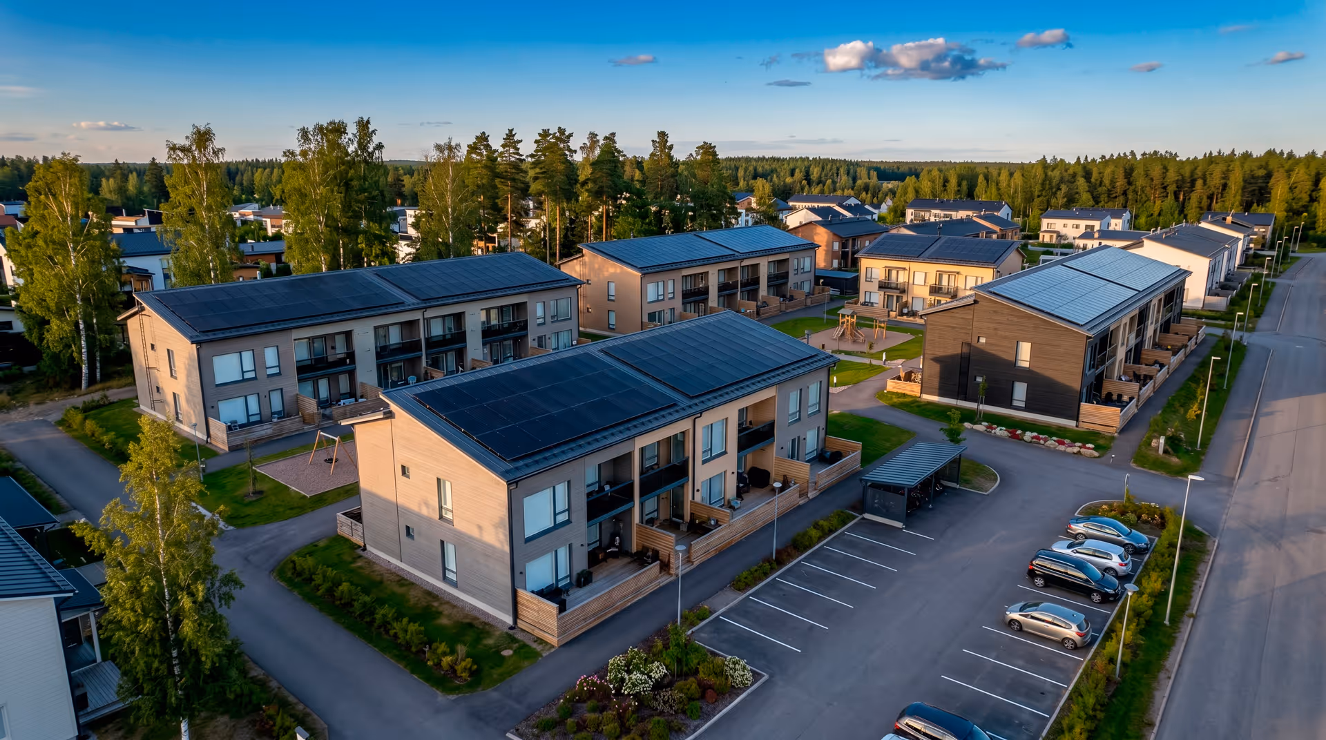 Taloyhtiön asuinrakennuksia, joissa on aurinkopaneelit katoilla, aurinkoisessa ja vehreässä ympäristössä.