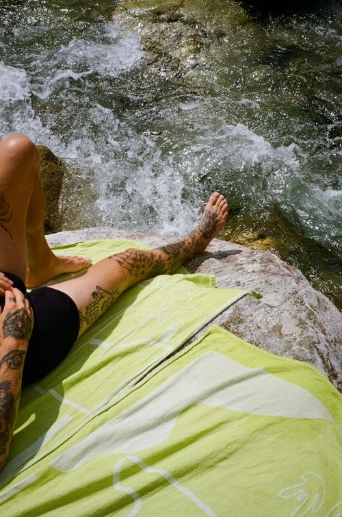 A Handsome man pictured sun bathing on the Sun Tales Beach Towel, a sustainable beach towel produced in small quantities, made in Spain.