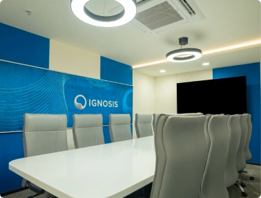 Modern conference room with white table, gray chairs, ceiling lights, and Ignosis logo on blue wall at Ignosis AI office.