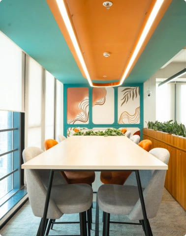 Modern Ignosis AI office meeting room with white table, gray and orange chairs, plants, and colorful ceiling accents.