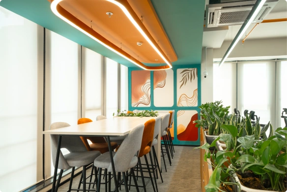 Modern Ignosis AI office meeting area with tall white table, mixed gray and orange chairs, plants, and colorful abstract wall art.