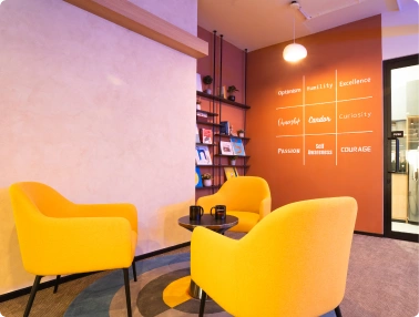 Office lounge with three yellow chairs around a small black table under a wall with motivational words at Ignosis AI.