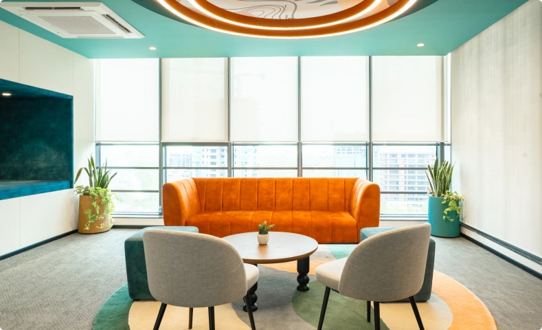 Bright lounge with orange sofa, round coffee table, gray chairs, plants, and large windows with blinds at Ignosis AI office.