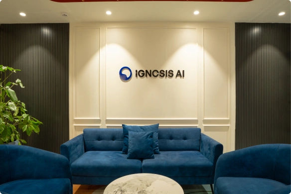 Modern Ignosis AI office lounge with blue velvet sofas, a marble table, green plant, and Ignosis AI logo on the wall.