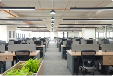 Modern room with an orange sofa, two gray chairs, round wooden table, and large windows with blinds at Manubhai & Shah LLP office.