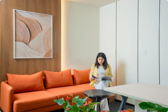 Modern Manubhai & Shah LLP office space with high white table, orange and gray chairs, green plants, and abstract wall art.