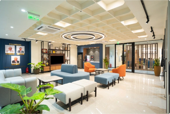 Modern Manubhai & Shah LLP office space with multiple desks, black chairs, blue dividers, and hanging lights under a decorated ceiling.