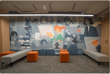Room with colorful mural of stylized people and three orange ottomans with gray benches at Manubhai & Shah LLP office.