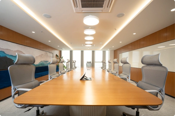 Modern conference room with wooden table, ergonomic office chairs, ceiling lights, and large windows at Manubhai & Shah LLP office.