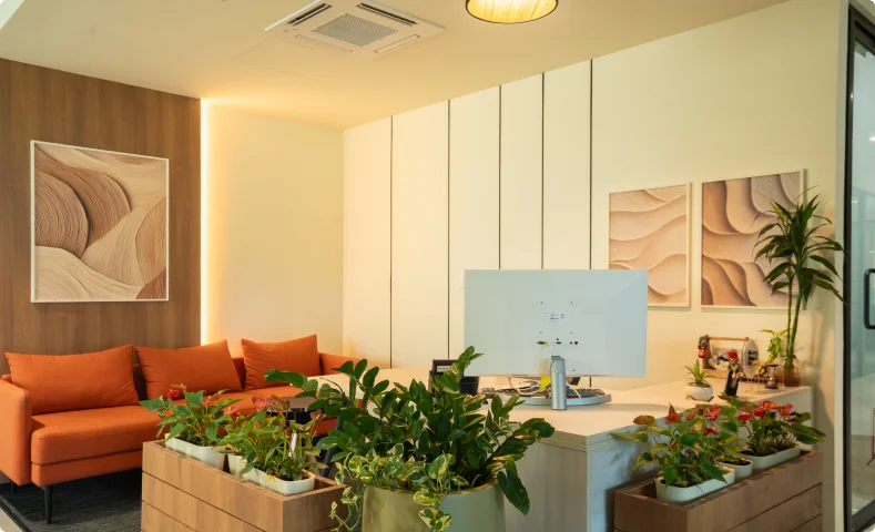 Modern Manubhai & Shah LLP office area with wooden walls, orange sofa, plants, desk, and computer monitor.