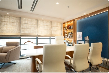 Modern Manubhai & Shah LLP office with white chairs around a wooden desk near windows with blinds and blue accent wall.