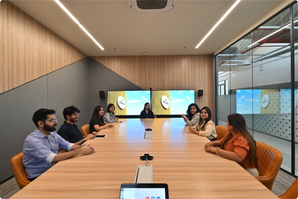 Seven people sitting around a long conference table in a modern meeting room with screens at Deakin University.