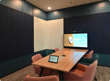 Deakin University modern conference room with a wooden table, pink and green chairs, digital display, and tablet on the table.