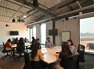 Team of people seated around two tables in a modern office with large windows at Deakin University.