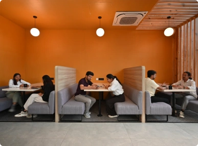 Three pairs of people seated at booths with orange walls and round ceiling lights in a modern cafe at Deakin University.