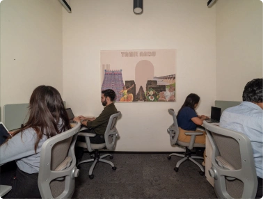 Four people working on laptops at desks in a small office with a travel-themed poster on the wall at Deakin University.