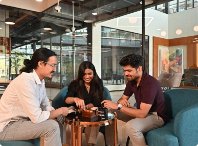Three people sitting around a small table playing a board game in a modern office lounge at Deakin University.