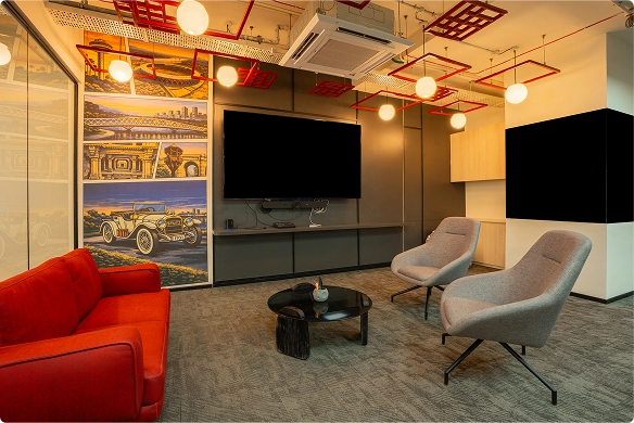 Walter P Moore modern lounge with red sofa, gray armchairs, round black table, and wall-mounted TV under ceiling lights.