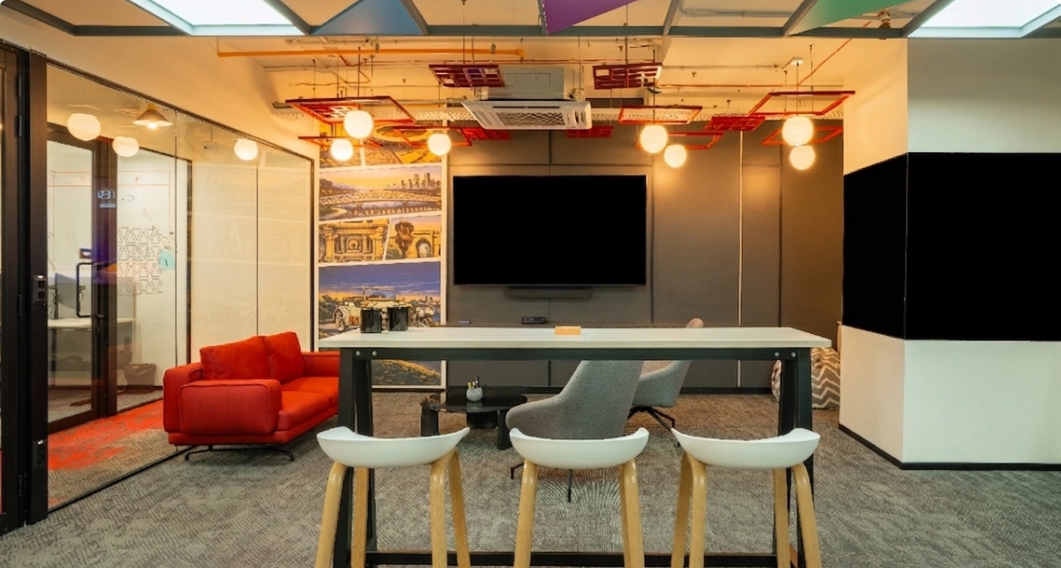 Walter P Moore modern office lounge with a red sofa, bar stools, gray chairs, and a large TV on the wall.
