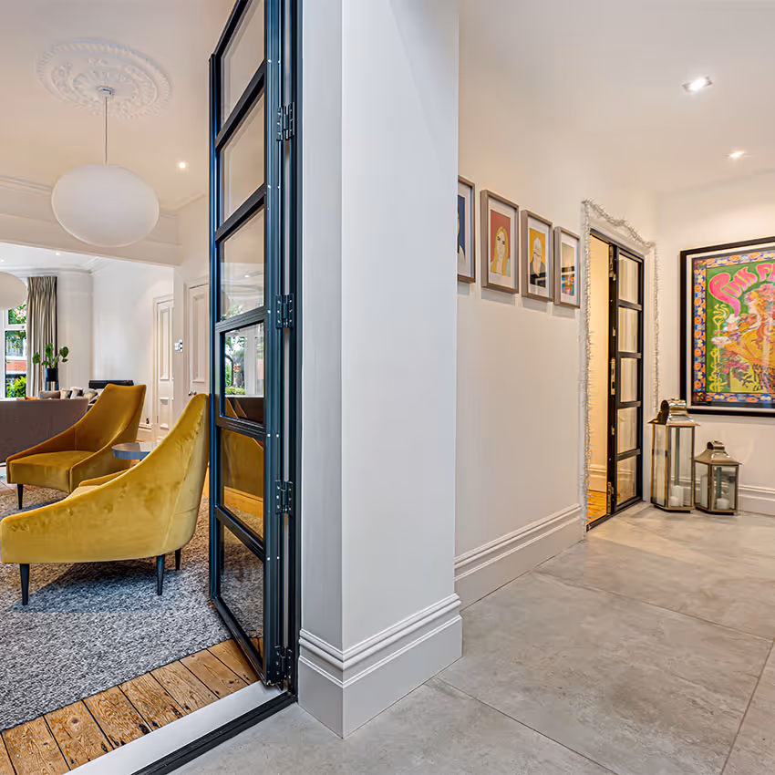 Black-framed double glazed steel-look external doors used internally, opening from tiled hallway into living space with wooden flooring.