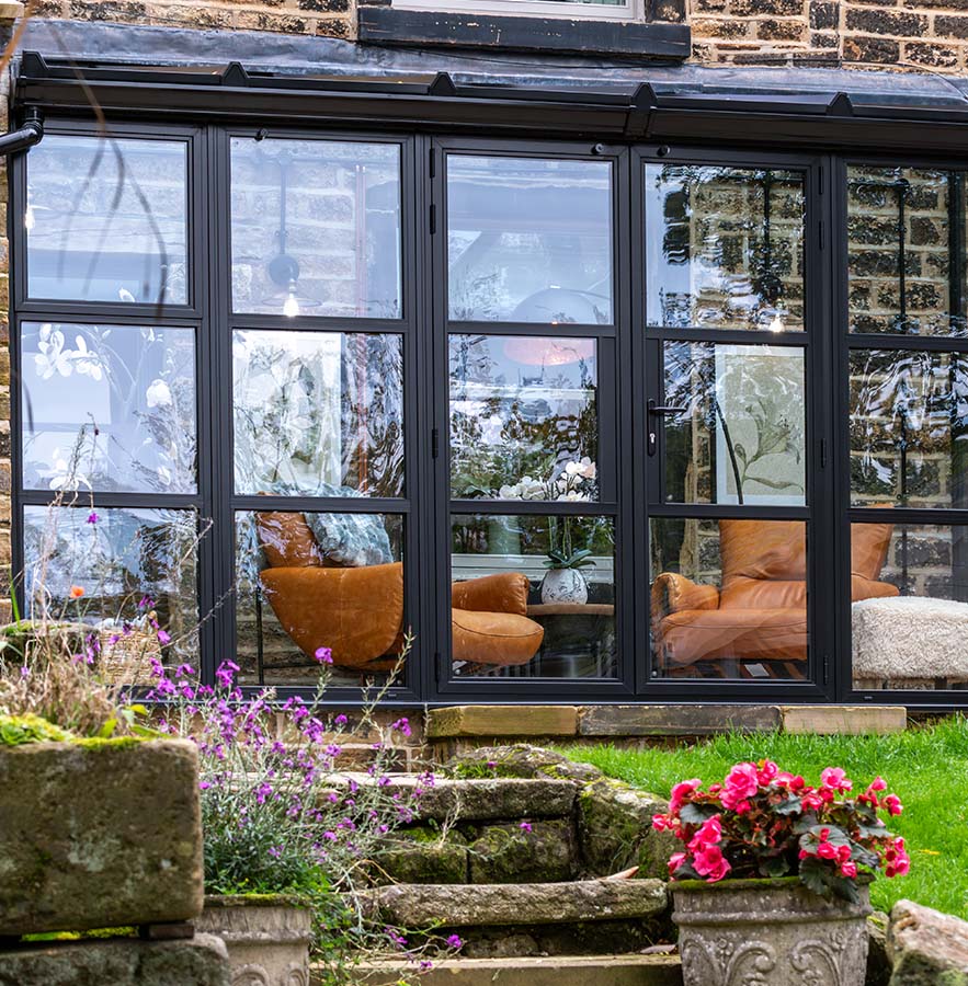 Black heritage-style aluminium doors and sidelights by Decorio fitted to a stone cottage, opening onto a garden with stone step