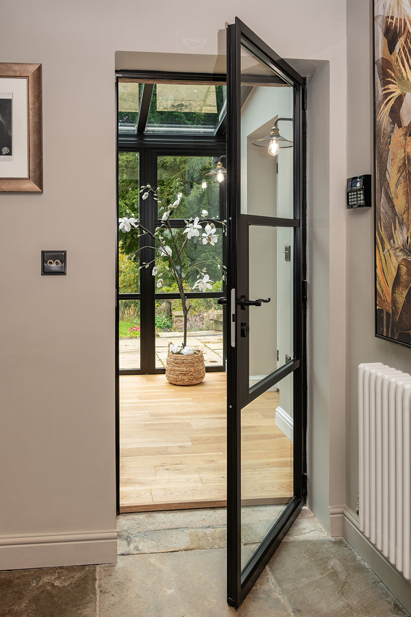 Black heritage-style aluminium doors and sidelights by Decorio fitted to a stone cottage, opening onto a garden with stone step