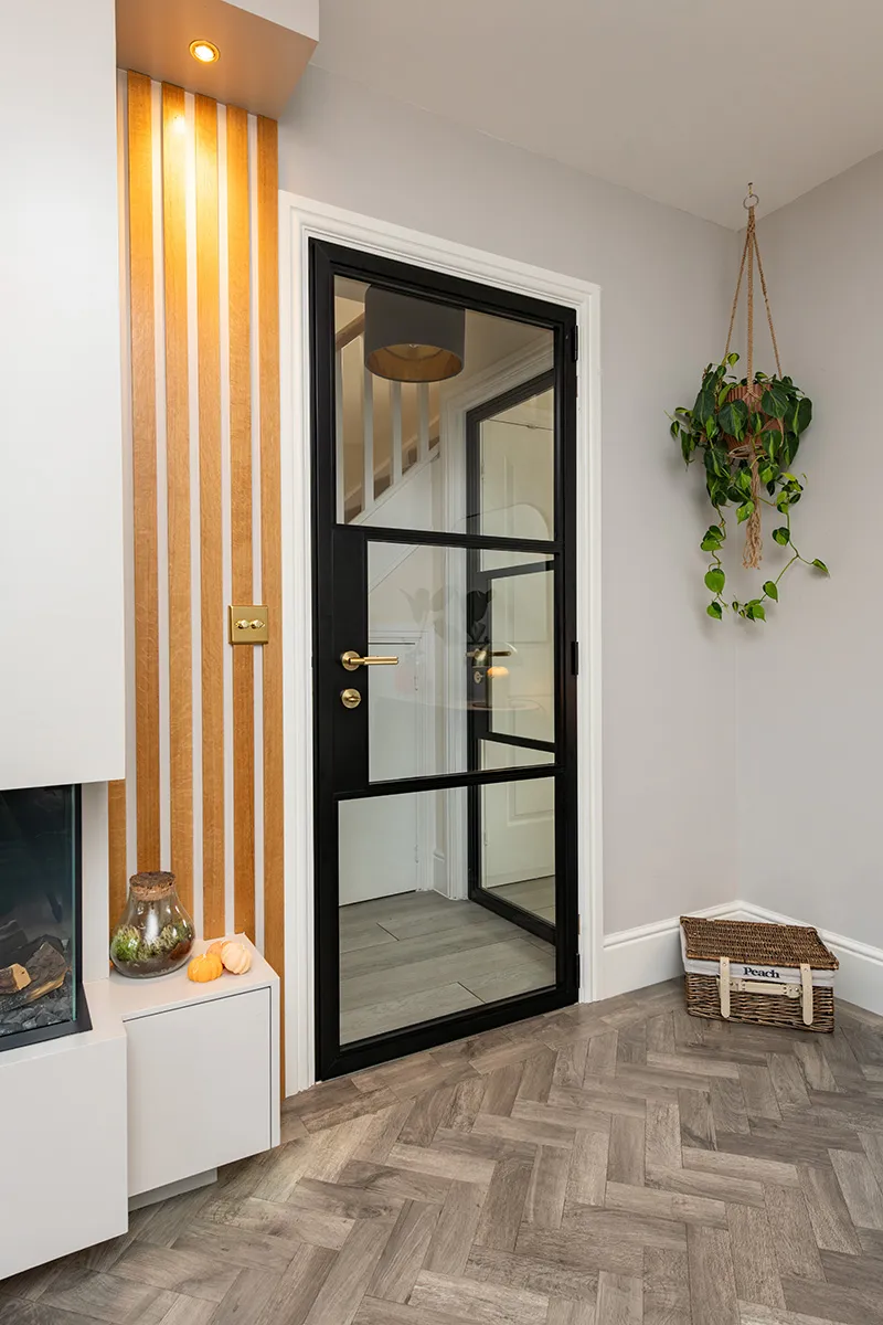 Black steel-look internal hinged door by Decorio with gold handle, installed in a stylish hallway featuring wood panelling and herringbone flooring