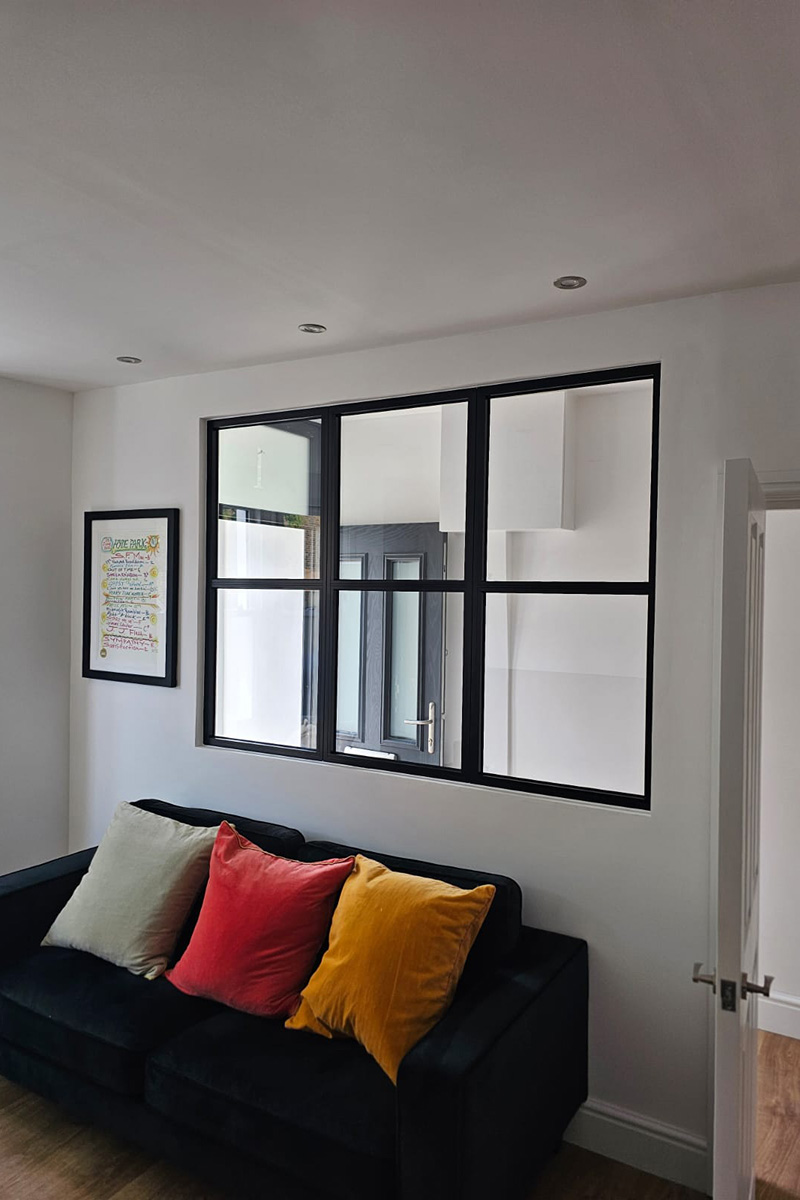 Black steel-look internal screen by Decorio installed above a sofa in a modern living space, creating a stylish partition with a matching door beyond