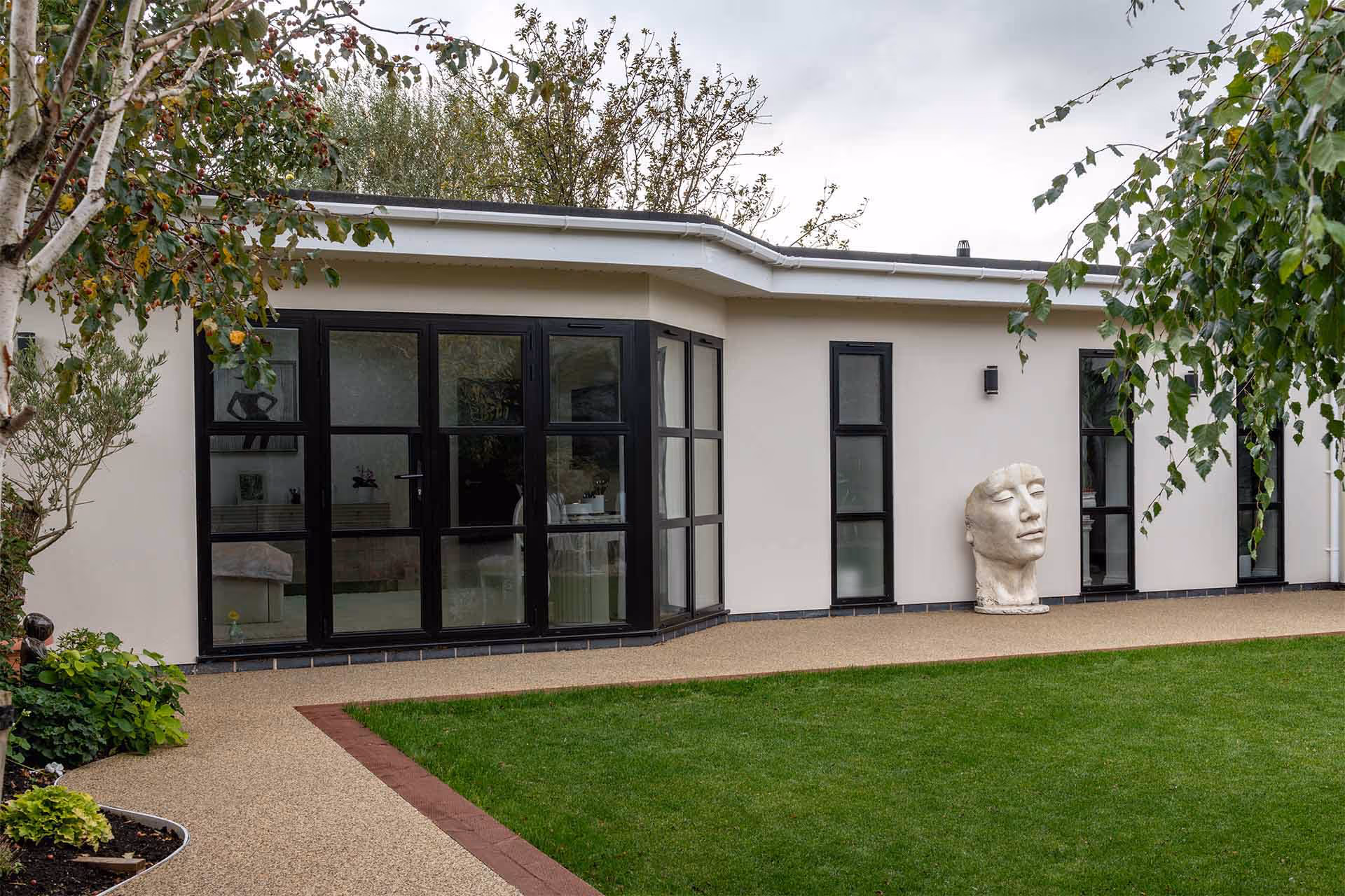 Black crittal-style aluminium doors and windows by Decorio installed on a modern cream-rendered home with landscaped garden and contemporary sculpture