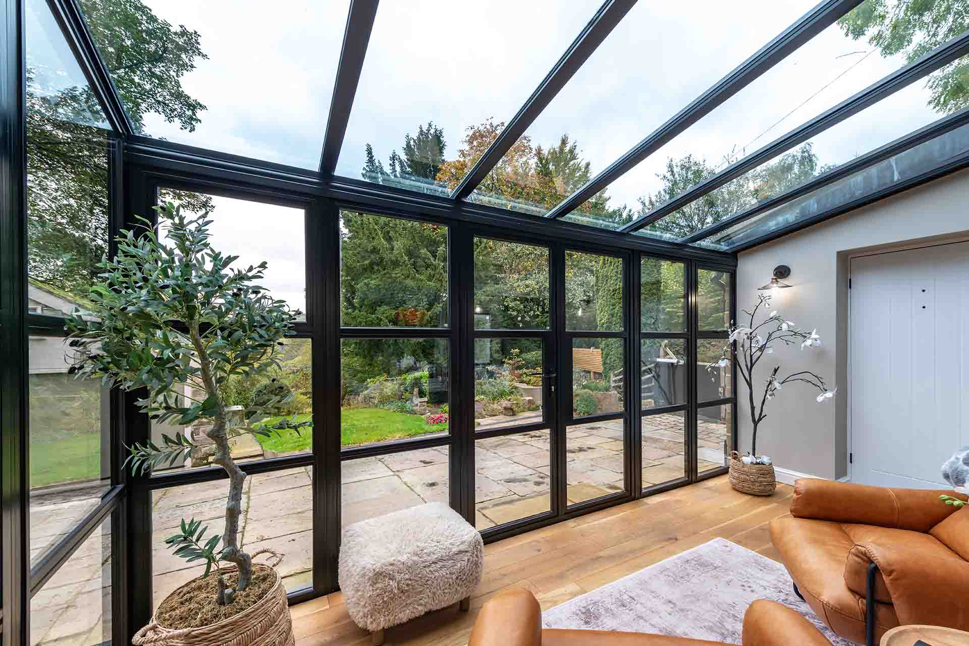 Elegant black aluminium heritage doors and glazing by Decorio forming a bright garden room with a glass roof, opening out to a stone patio and landscaped garden