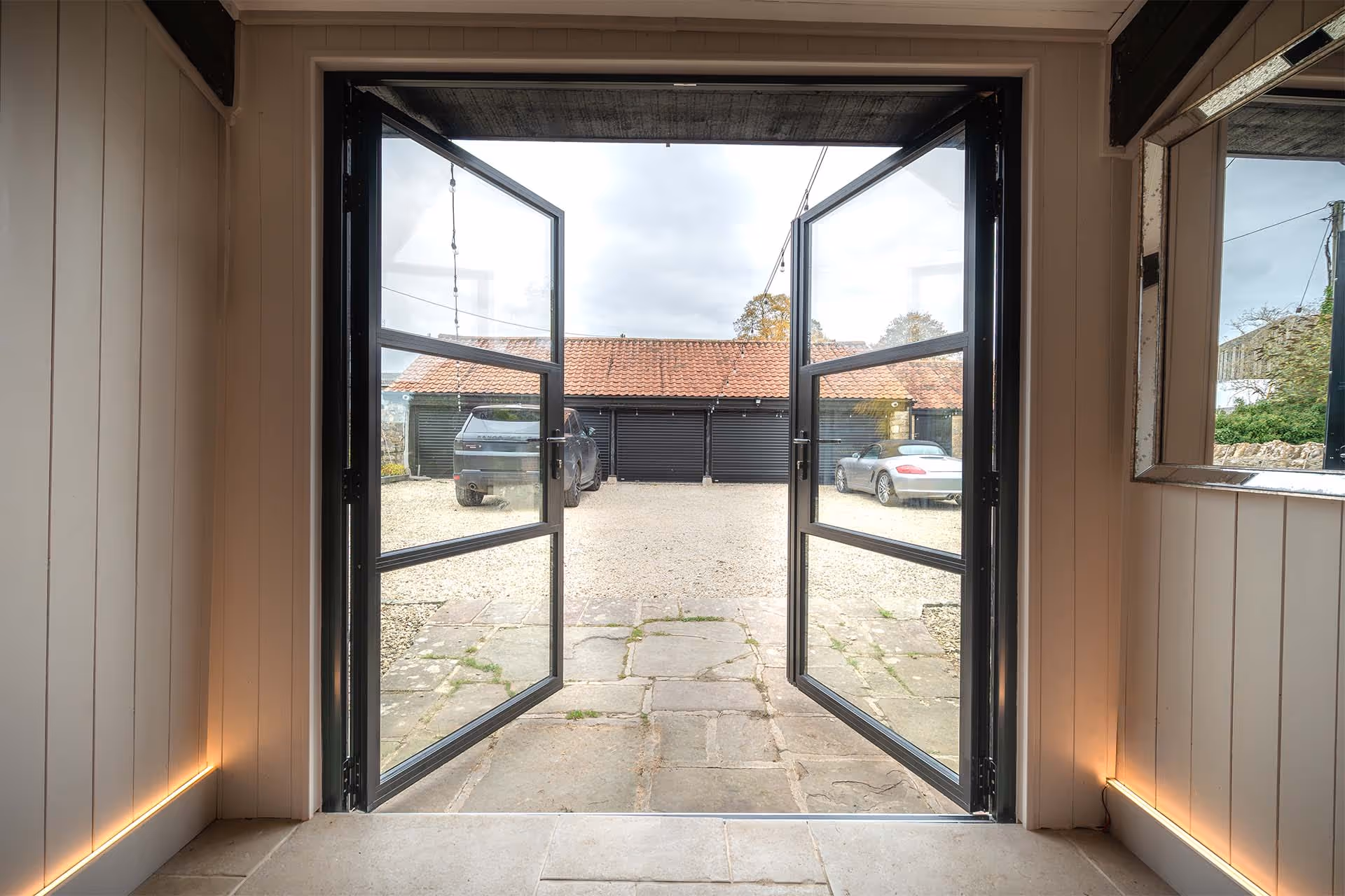 Interior view through Decorio heritage-style French doors opening onto a traditional courtyard with stone paving and barn-style buildings