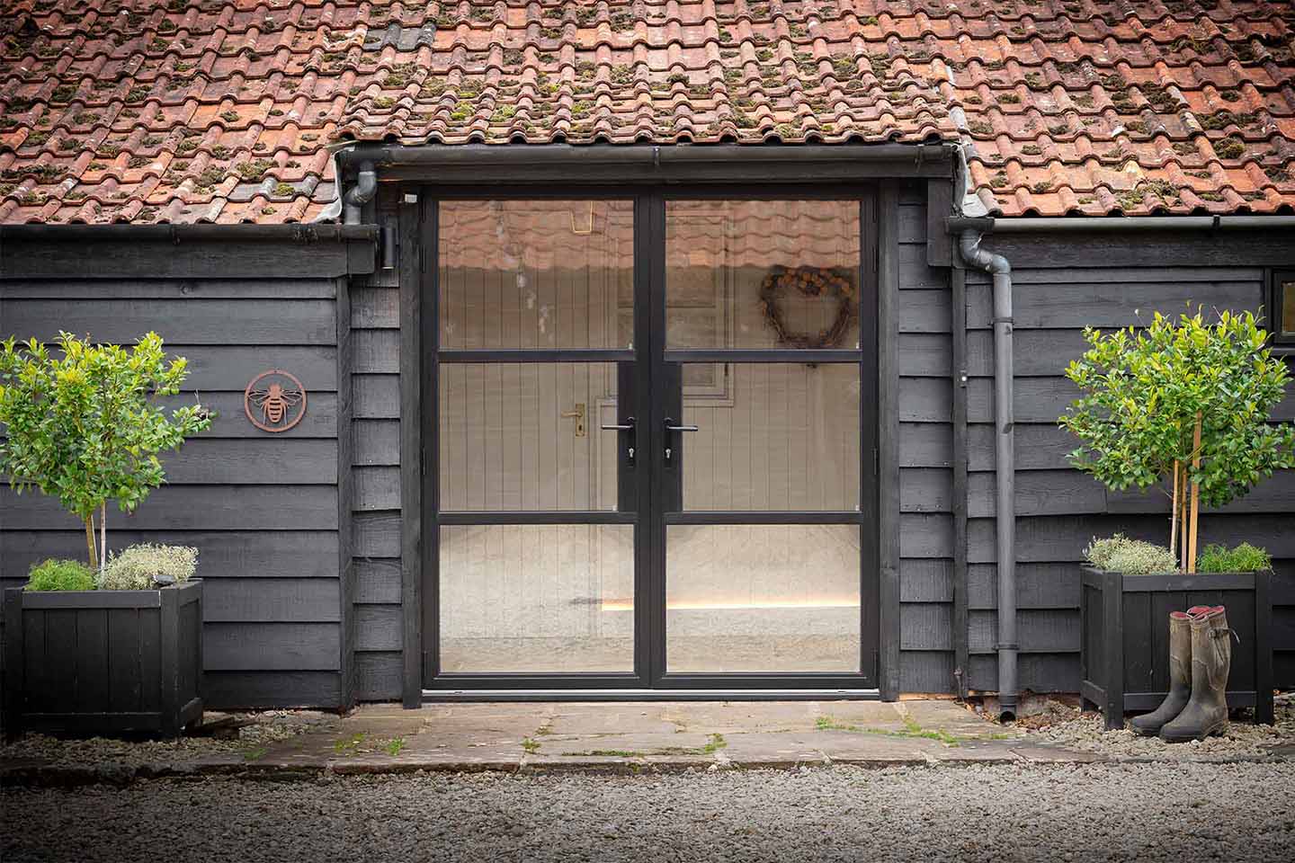 Black heritage-style aluminium French doors by Decorio fitted to a rustic barn with timber cladding and a weathered clay tile roof