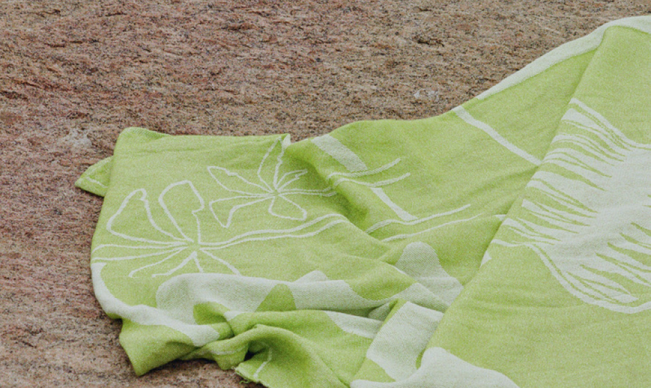 Sun Tales is a sustainable lime coloured beach towel, this shows a detail, the corner of the beach towel on the rocks 