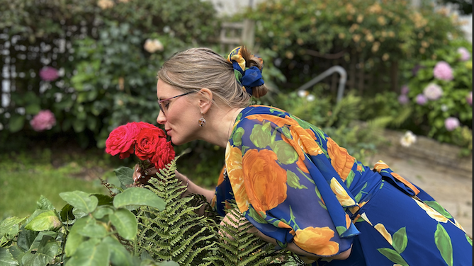 Grethe pausing to smell roses during a seasonal Lughnasadh ritual, honoring nature’s beauty and late-summer abundance.