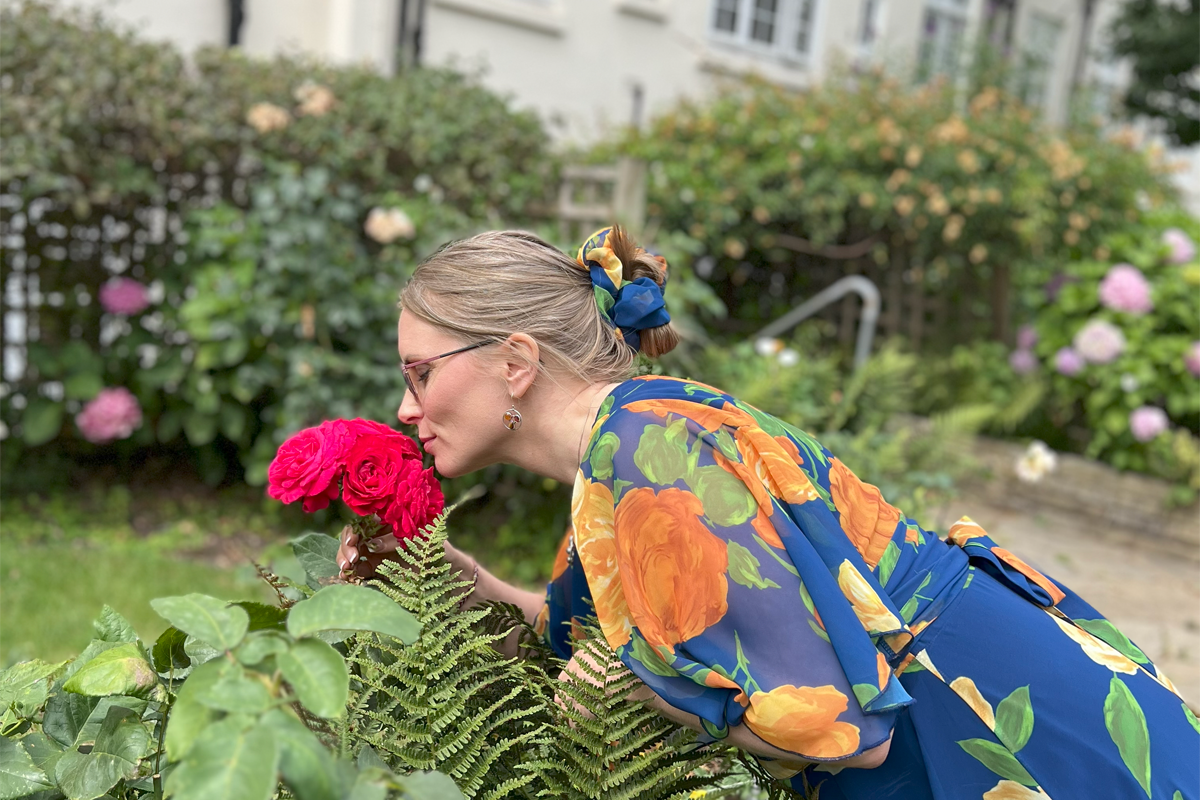 Grethe pausing to smell roses during a seasonal Lughnasadh ritual, honoring nature’s beauty and late-summer abundance.
