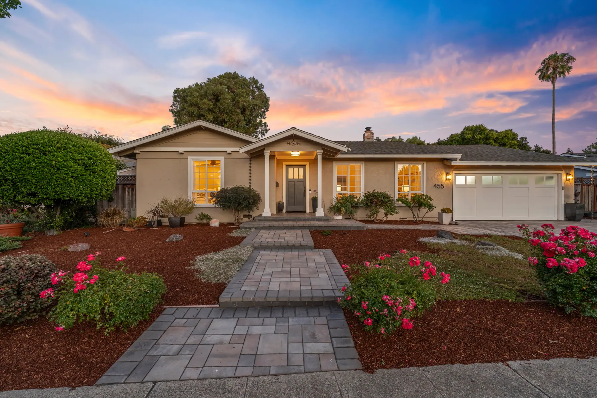 Single-story home glowing at dusk with a landscaped front yard and rose bushes