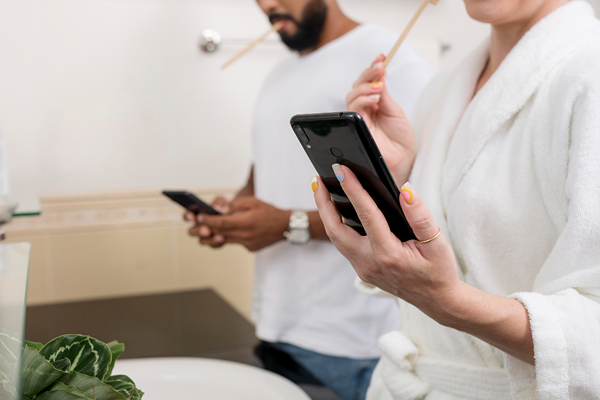 Couple in a bathroom brushing their teeth while looking at their phones.