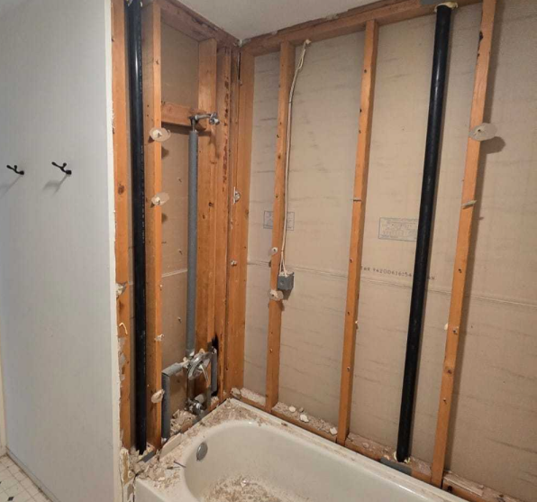 Exposed plumbing and pipes in a shower wall after demolition, ready for inspection and updating during a renovation.
