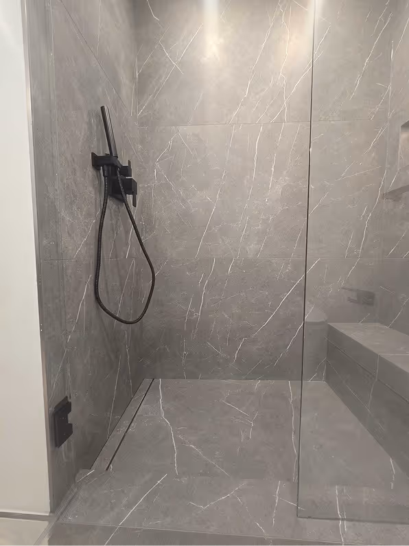 Modern walk-in shower with large gray porcelain tiles, a built-in bench, and a sleek black linear drain.