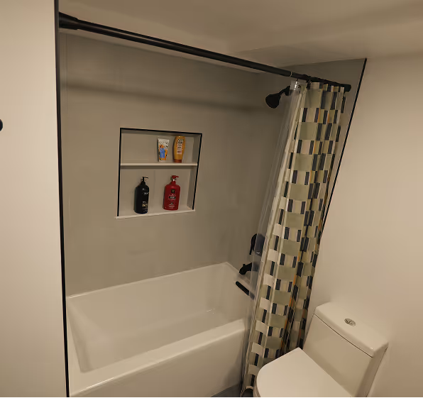 A new bathtub and shower with a custom-built, recessed tile niche for storing shampoo and soap bottles.