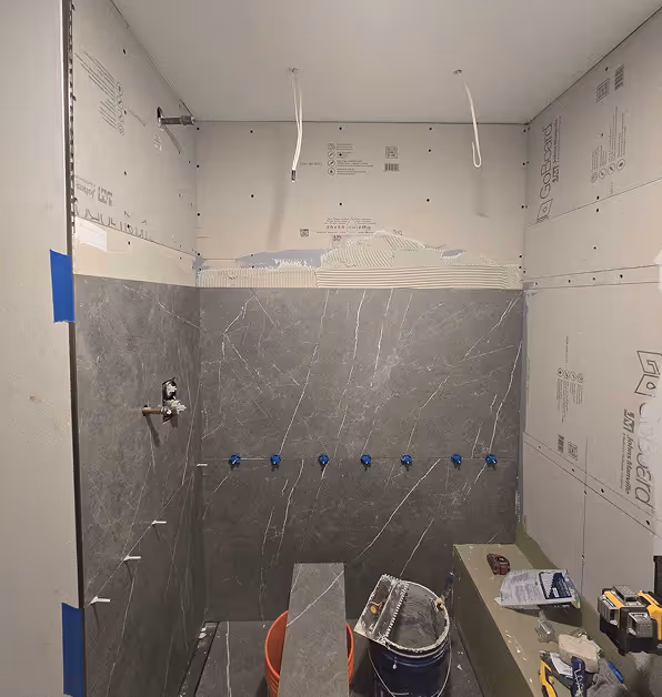 A shower mid-remodel, showing large gray tiles being installed over a waterproof backer board system.