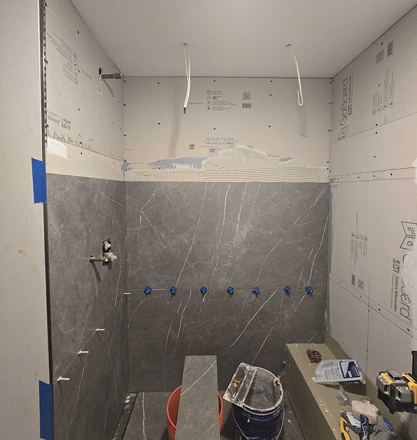A shower mid-renovation, showing large gray tiles being installed over a waterproof backer board system.