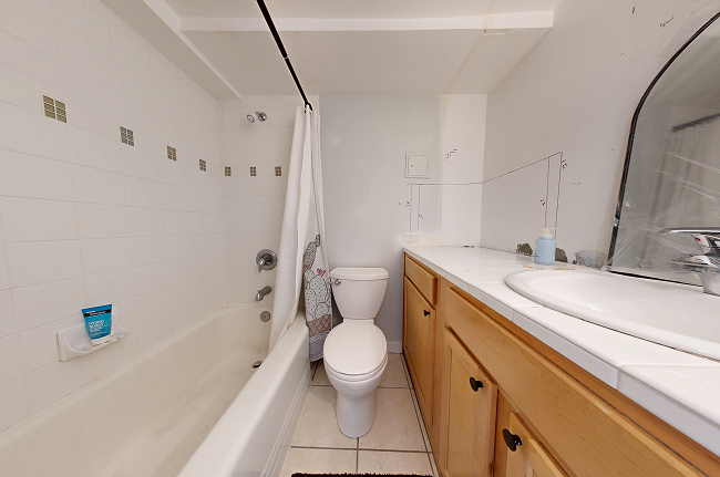Small outdated bathroom with wood vanity, large mirror, and hidden water heater.
