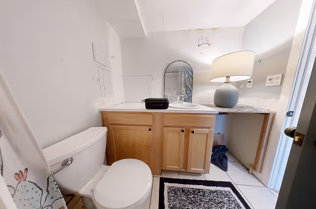 Outdated wood vanity with cluttered countertop, mirror, and toilet in small bathroom.