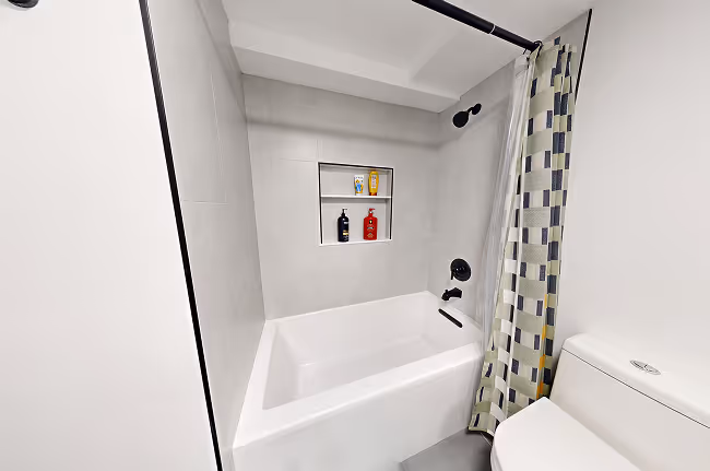 Modern tub and shower with gray tile walls, black fixtures, and built-in storage niche.