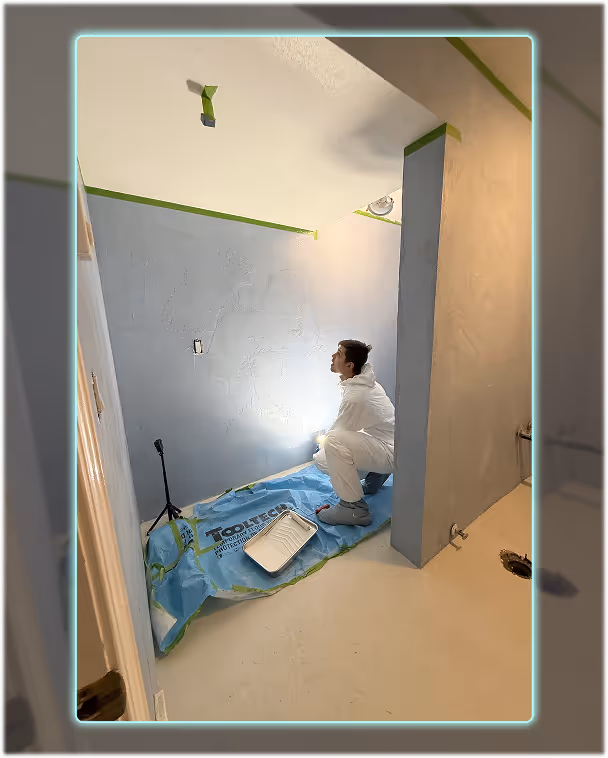 Worker in protective gear sealing microcement walls in a bathroom during the final stages.