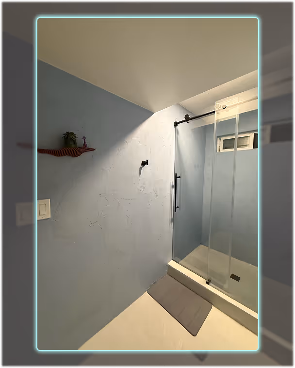 Finished microcement shower with soft blue walls, glass door, and a smooth seamless floor.