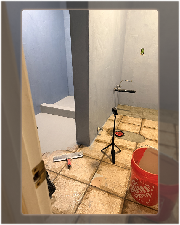 Microcement application in progress with freshly coated walls and exposed floor tiles during renovation.