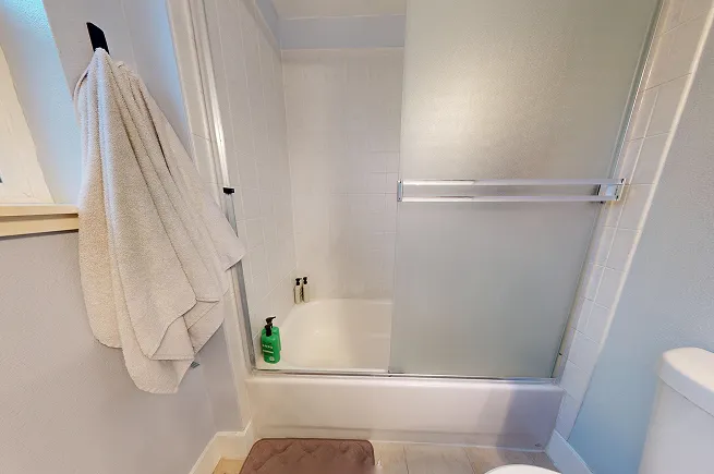 Original tub-shower combo with sliding glass door and white tile surround before microcement conversion in West Seattle.